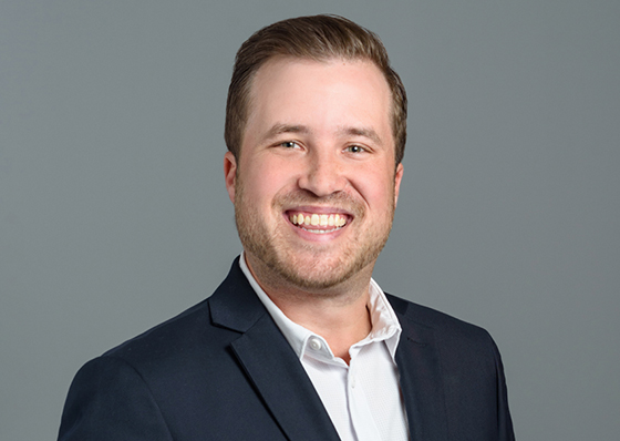 A man, Matthew Richards,  in a blue suit jacket and a white collared shirt.